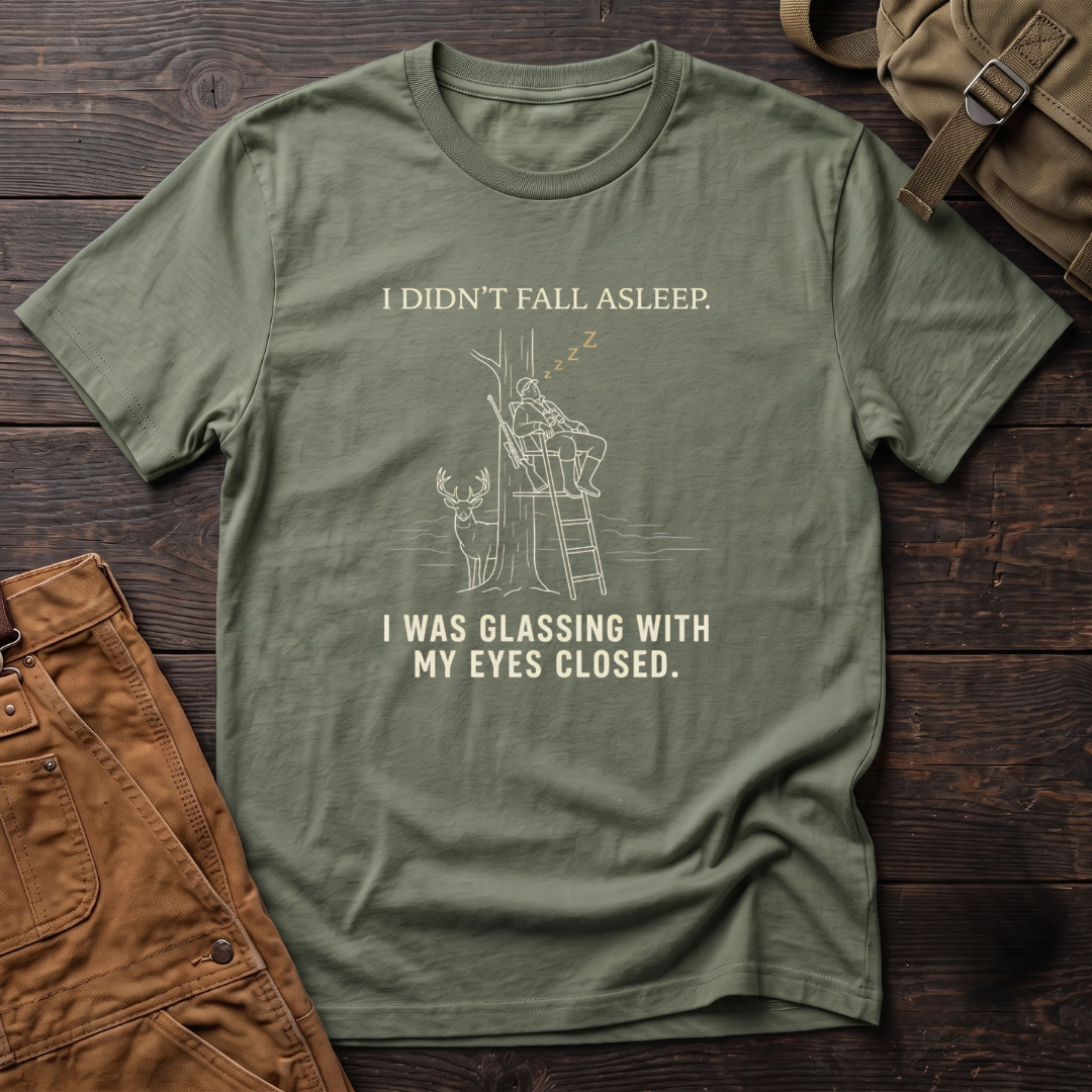 Military Green funny deer hunting t-shirt with I Didn't Fall Asleep, I Was Glassing With My Eyes Closed text and a line-art hunter dozing in a ladder stand while a whitetail buck stands below