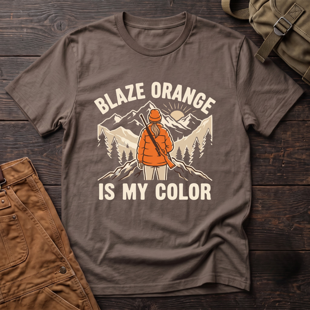 Brown women's hunting t-shirt with Blaze Orange Is My Color lettering and a woman hunter in blaze orange with a rifle facing a mountain sunrise