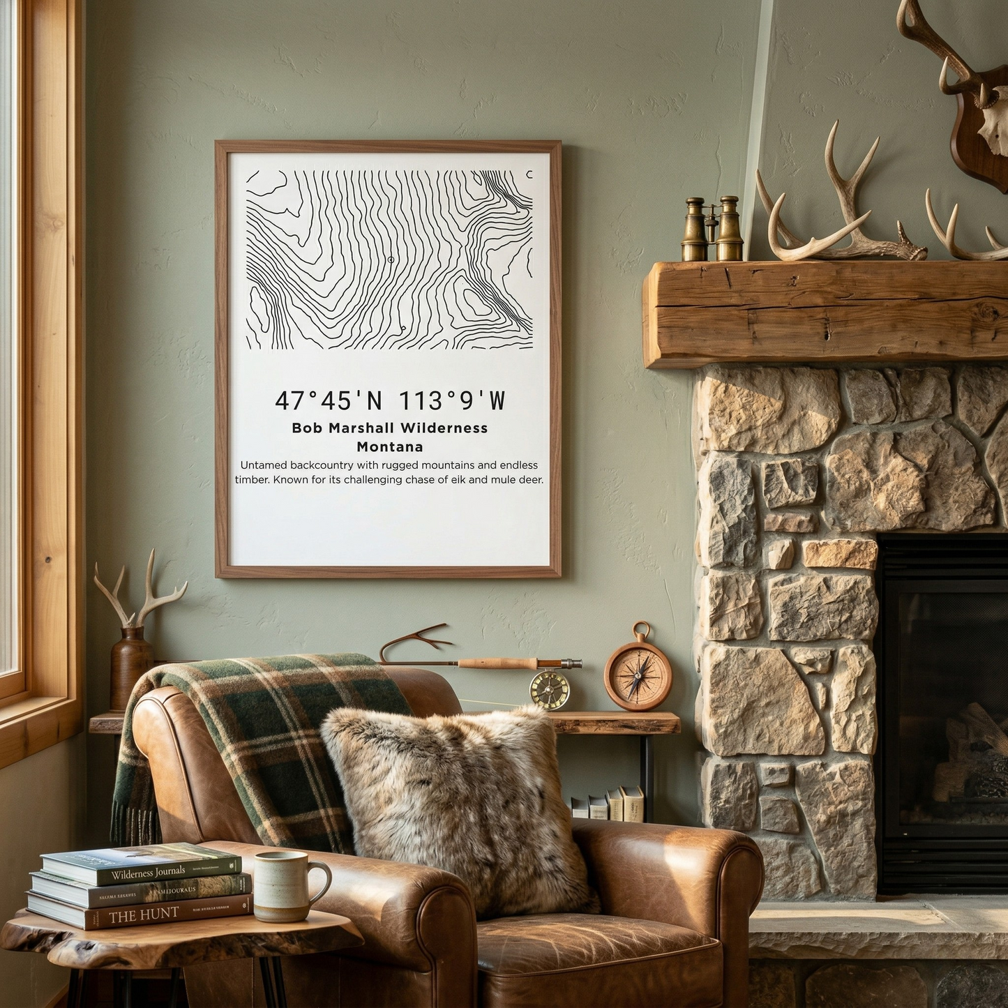 A minimalist Bob Marshall Wilderness Montana topographic map poster displayed in a walnut frame above a stone fireplace in a rustic hunting lodge, surrounded by elk antlers, binoculars, a fly rod, and leather furniture.