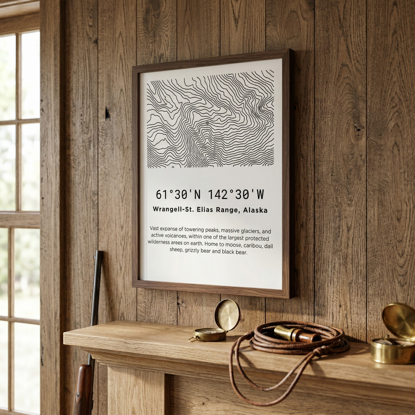 A minimalist Wrangell-St. Elias Range Alaska topographic map poster displayed in a walnut frame on a rustic wood-plank cabin wall above a shelf with brass compass, leather binoculars, and a rifle leaning against the wall.