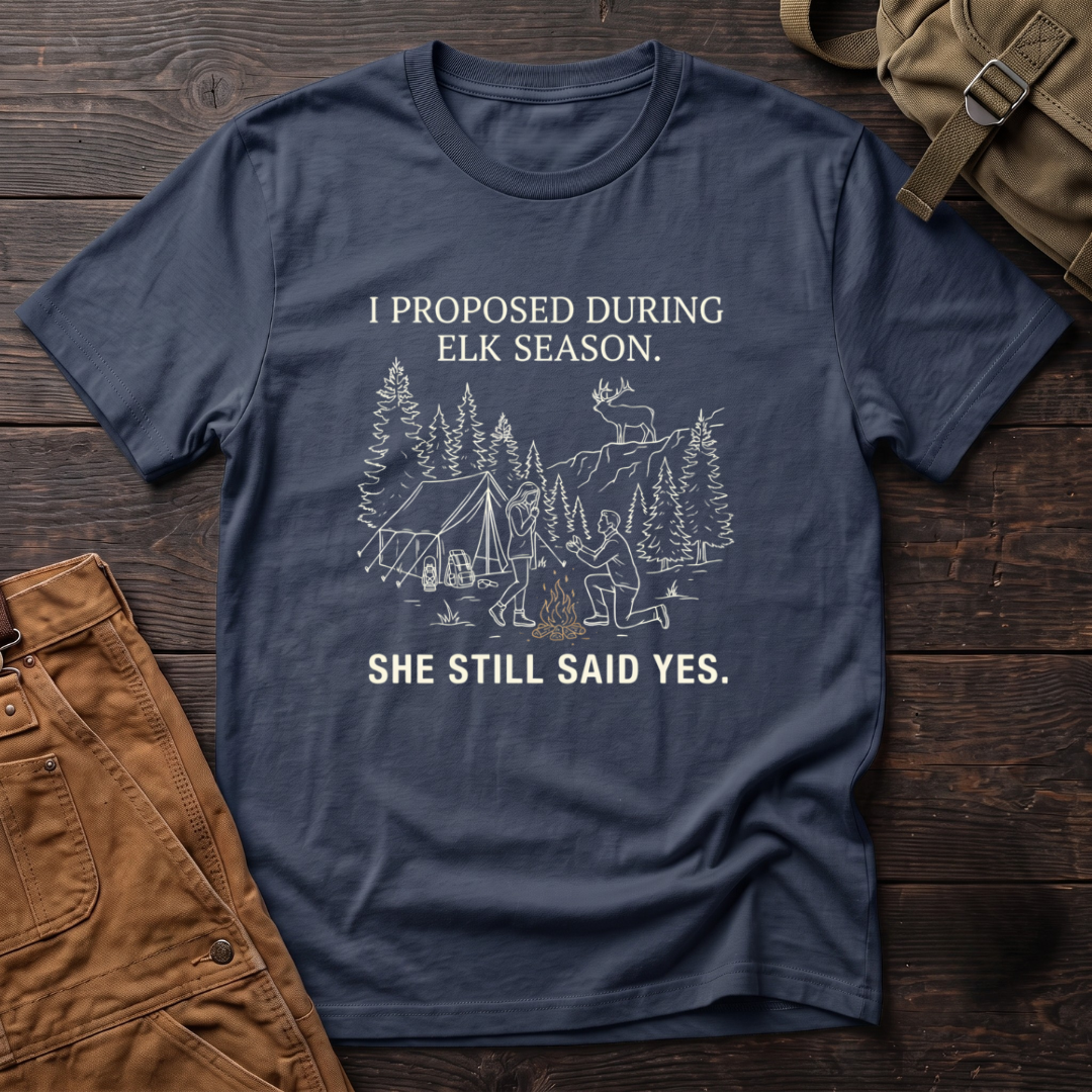 Navy funny elk hunting t-shirt with I Proposed During Elk Season, She Still Said Yes text and a line-art hunter kneeling by the campfire at an elk camp tent, with a bull elk on the ridge