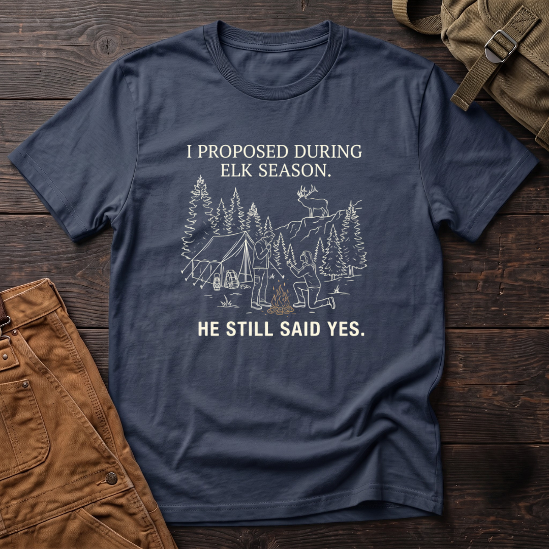 Navy funny elk hunting t-shirt with I Proposed During Elk Season, He Still Said Yes text and a line-art hunter kneeling by the campfire at an elk camp tent, with a bull elk on the ridge