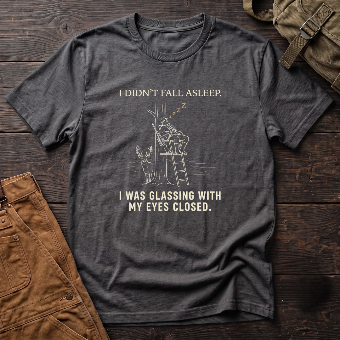 Asphalt funny deer hunting t-shirt with I Didn't Fall Asleep, I Was Glassing With My Eyes Closed text and a line-art hunter dozing in a ladder stand while a whitetail buck stands below