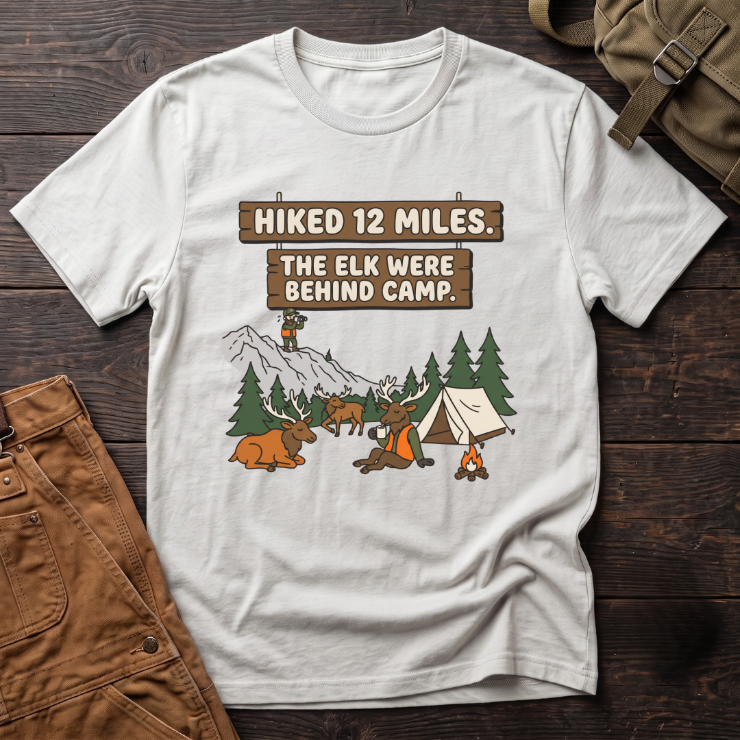 White funny elk hunting t-shirt with Hiked 12 Miles. The Elk Were Behind Camp. signs and elk walking past a tent while the hunter glasses far away