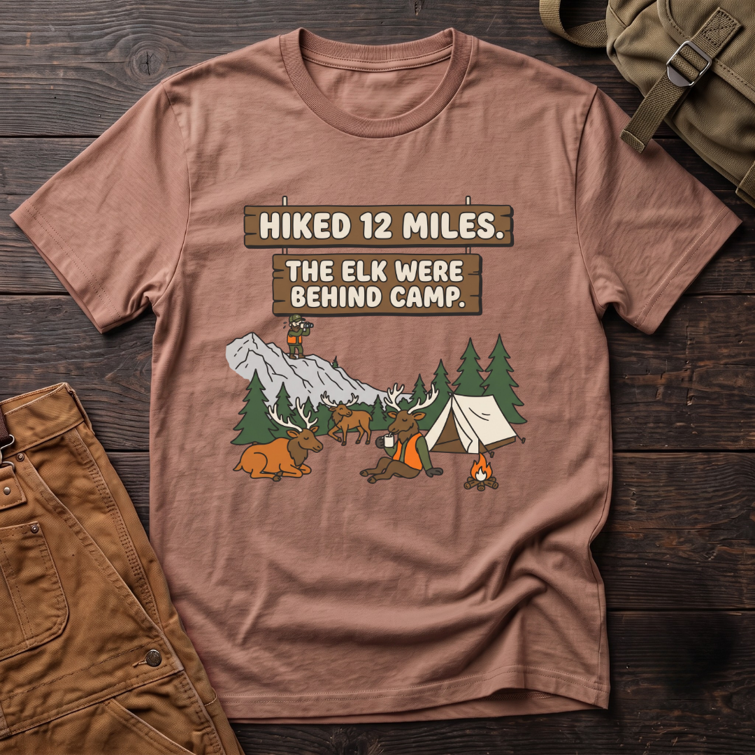 Heather Clay funny elk hunting t-shirt with Hiked 12 Miles. The Elk Were Behind Camp. signs and elk walking past a tent while the hunter glasses far away