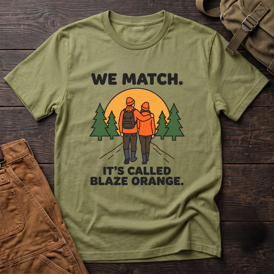 Heather Green funny hunting couple t-shirt with We Match. It's Called Blaze Orange. text and a hunting couple in blaze orange walking toward a sunset between pine trees