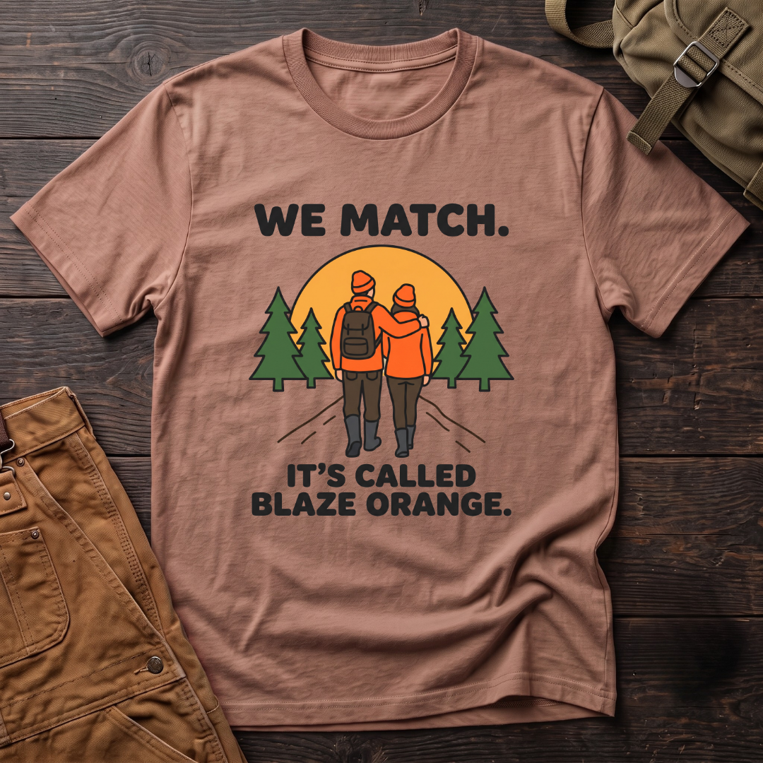 Heather Clay funny hunting couple t-shirt with We Match. It's Called Blaze Orange. text and a hunting couple in blaze orange walking toward a sunset between pine trees
