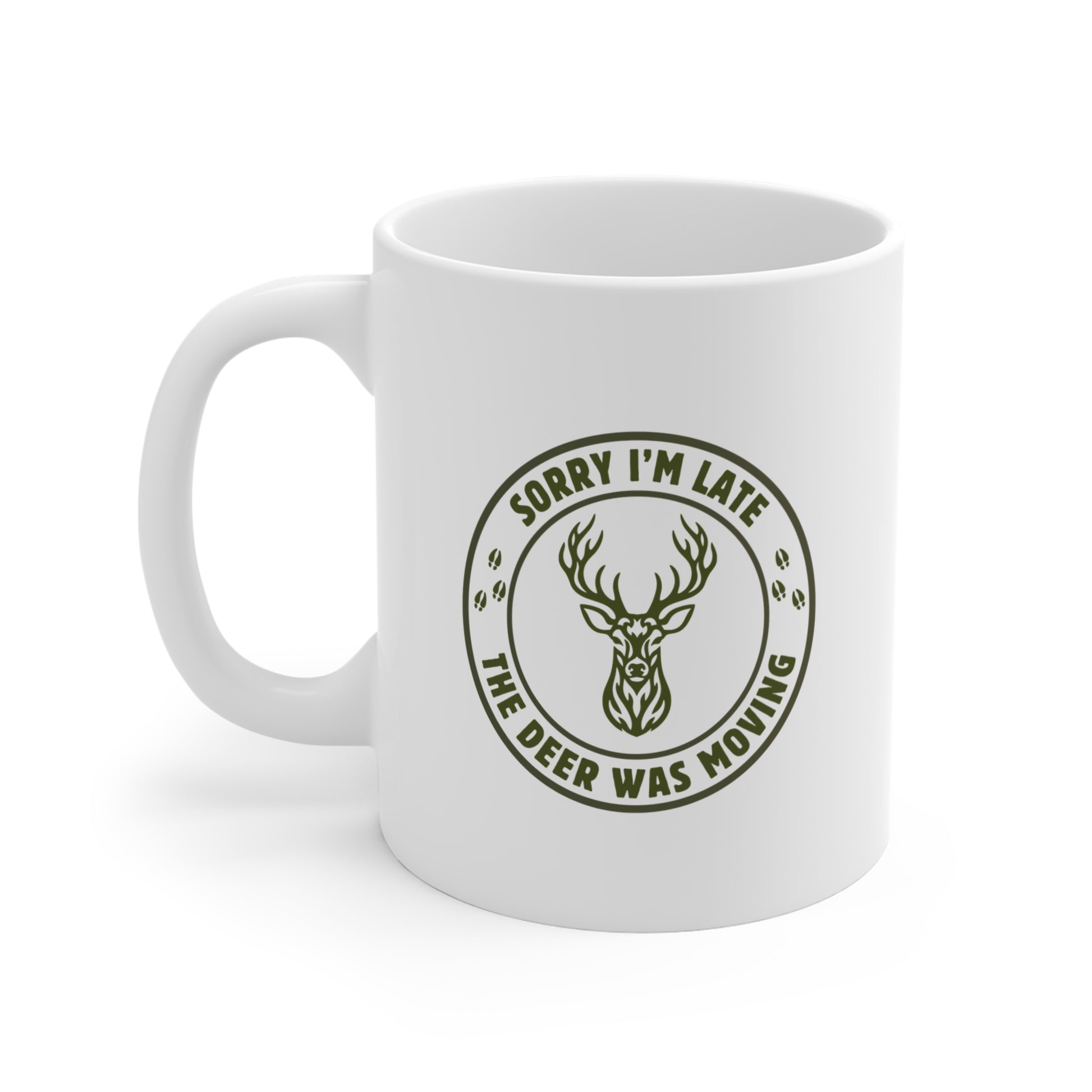 White ceramic hunting mug with a funny Sorry I'm Late the Deer Was Moving slogan and tribal whitetail deer badge graphic in olive green, shown from the left side on a white background.